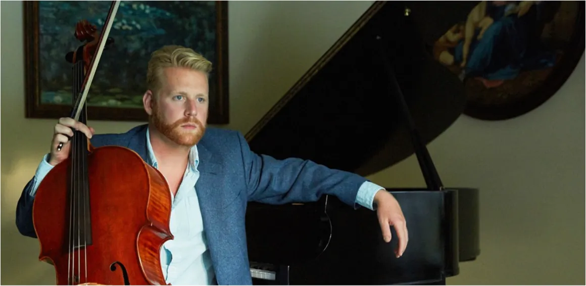 Cellist Daniel Grab seated with his cello beside a grand piano