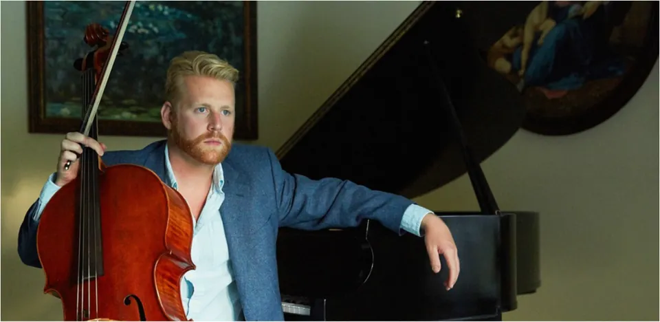 Portrait of cellist Daniel Grab with his cello beside a piano