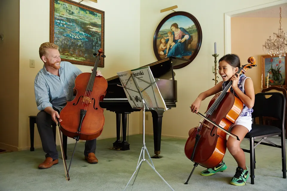 Daniel Grab laughing with a young cello student during a lesson beside a grand piano
